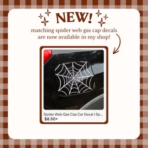 May include: A white spider web decal applied to a black vehicle fuel filler cap. The image includes the text NEW! matching spider web gas cap decals are now available in my shop! and Spider Web Gas Cap Car Decal | Sp... with a brown arrow pointing to the decal.