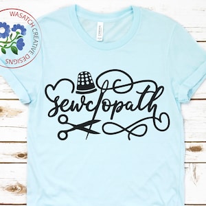 May include: A light blue t-shirt with black text that reads "Sewcopath" with a thimble, scissors, and a decorative swirl design.