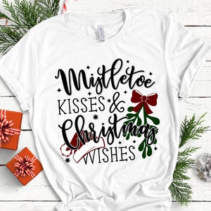 May include: White t-shirt with a black graphic design that says "Mistletoe Kisses & Christmas Wishes". The graphic includes a red bow, green mistletoe, and a red Santa hat.