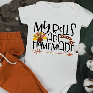 May include: White baby onesie with a brown turkey graphic and the text "My rolls are homemade".