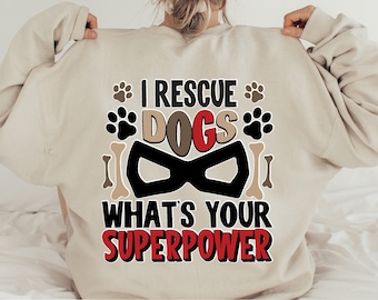 May include: A beige sweatshirt with the text "I rescue dogs what's your superpower" in black and red lettering. The text is surrounded by paw prints and bone graphics.