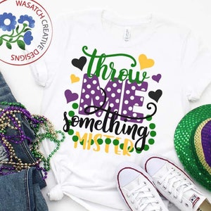 May include: White t-shirt with the text "Throw Me Something Mister" in black, green, purple, and yellow. The text is surrounded by polka dots and hearts.