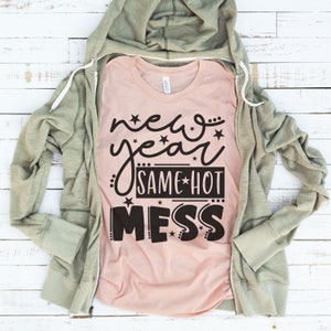 May include: A pink t-shirt with a black graphic that says "new year same hot mess" with stars around the text.