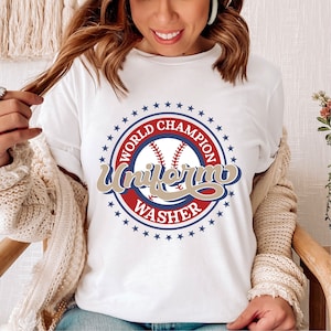 Puede incluir: Camiseta blanca con un gráfico de béisbol azul, rojo y dorado que dice "World Champion Uniform Washer".