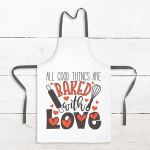 Peut inclure: Tablier blanc avec des bretelles noires et le texte "All good things are baked with love" en noir avec un motif de c&oelig;ur rouge. Un rouleau &agrave; p&acirc;tisserie et un fouet sont illustr&eacute;s de chaque c&ocirc;t&eacute; du texte.