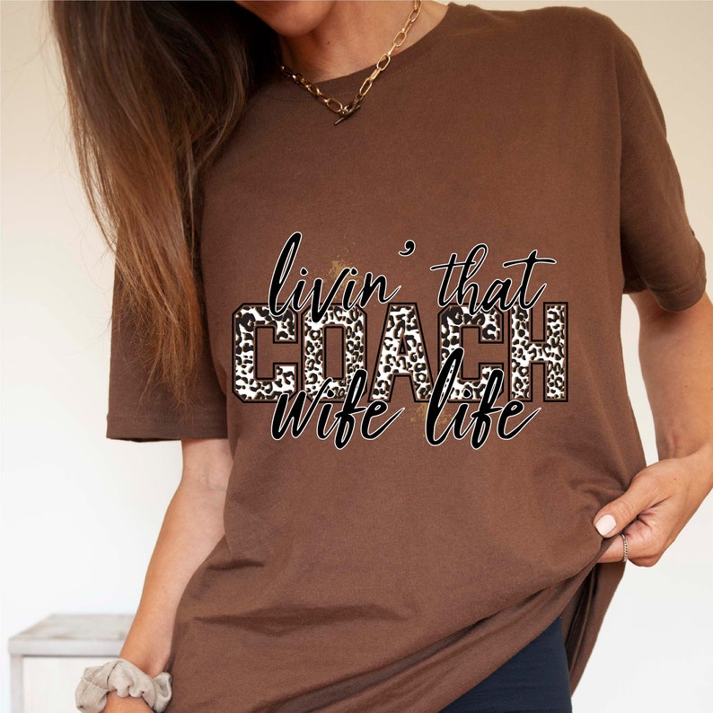 Peut inclure: T-shirt marron avec un motif l&eacute;opard qui dit "livin' that COACH wife life" en texte noir.