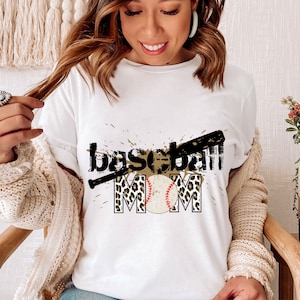 Peut inclure: T-shirt blanc avec un motif graphique noir et marron qui dit "baseball mom" avec un ballon de baseball et une batte de baseball.