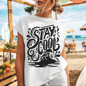 以下が含まれることがあります： 黒い「STAY COOL」の文字が特徴的な白いTシャツ。波と水滴のグラフィックデザイン。ビーチで着用されています。
