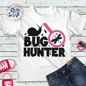May include: White t-shirt with a black and pink design. The design features a snail, a magnifying glass with a dragonfly inside, and the text "BUG HUNTER".