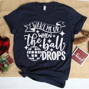 May include: A navy blue t-shirt with the text "Wake me up when the ball drops" in white. A white disco ball graphic is included in the text.