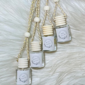 Peut inclure: Quatre petites bouteilles en verre avec des étiquettes blanches et des cordons dorés. Les étiquettes ont du texte noir et un motif floral. Les bouteilles sont remplies d'un liquide clair. Les parfums sont : Récolte de pommes, Jamaïque me rend fou, Cerise noire et Sucre rose.