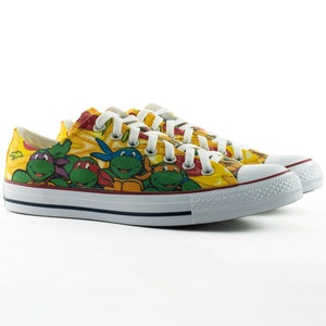 May include: A pair of yellow canvas sneakers with a Teenage Mutant Ninja Turtles print. The sneakers have white laces and a white rubber sole.