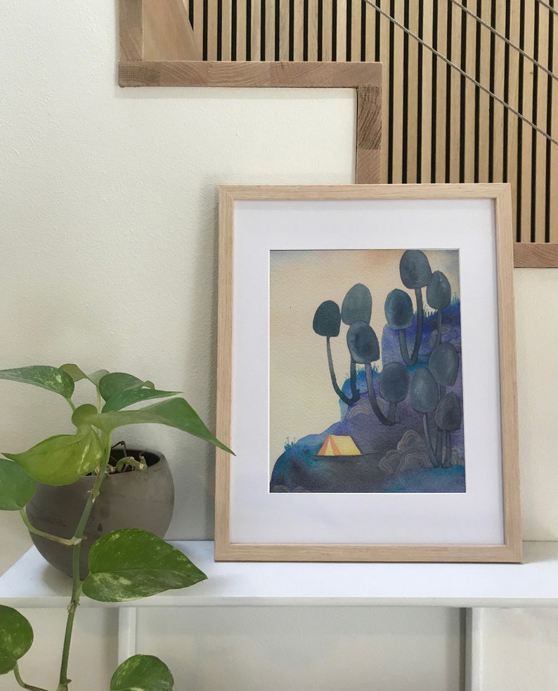 May include: A framed watercolor painting of a forest scene with a small yellow tent in the foreground. The trees are stylized and have a blue-grey color. The background is a gradient of blue and purple.
