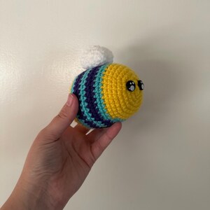 Puede incluir: Una abeja de ganchillo con rayas amarillas, turquesas y moradas. La abeja tiene grandes ojos negros y un peque&ntilde;o copo blanco en la espalda. Este art&iacute;culo hecho a mano es una pieza decorativa linda y caprichosa.