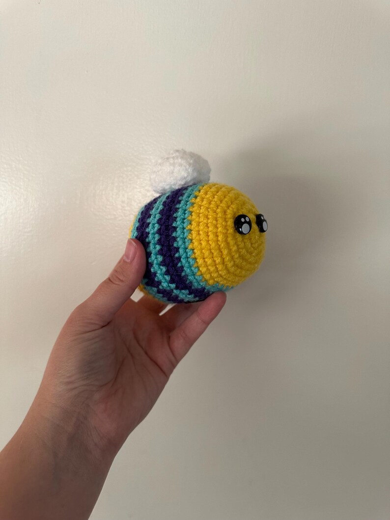 Puede incluir: Una abeja de ganchillo con rayas amarillas, turquesas y moradas. La abeja tiene grandes ojos negros y un peque&ntilde;o copo blanco en la espalda. Este art&iacute;culo hecho a mano es una pieza decorativa linda y caprichosa.