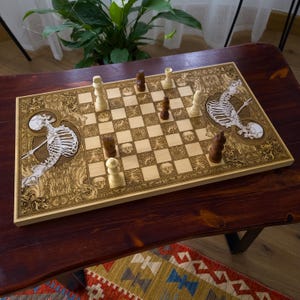 May include: A wooden chess set with a unique skeleton theme. The board features engraved artwork of skeletons and decorative patterns. The chess pieces are in light and dark wood tones. The board is on a dark wooden table.
