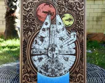 May include: A wooden plaque with an intricate design featuring a spaceship, two planets, and a blue background. The spaceship is a detailed illustration of the Millennium Falcon from Star Wars.