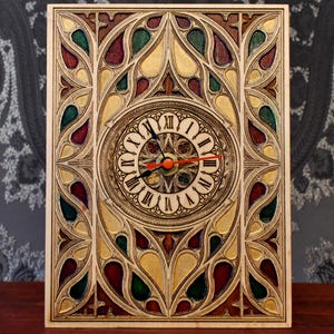 May include: A wooden clock with a stained glass design. The clock face has Roman numerals and red hands. The frame features a detailed, multi-coloured stained glass pattern in red, green, and gold.