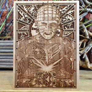 Könnte beinhalten: Ein Holzbrandbild eines Charakters aus dem Horrorfilm Hellraiser. Der Charakter trägt ein Metallkopfstück mit Stacheln und hält eine Rätselbox. Das Bild ist mit einem dekorativen Rahmen gerahmt.