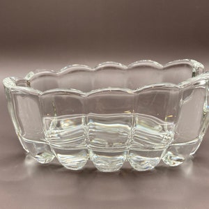 May include: A clear, rectangular glass bowl with a scalloped rim. The bowl has a grid-like pattern on the sides and a rounded base. The bowl is empty and sits on a neutral background.