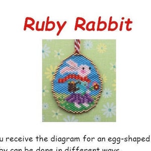 May include: A beaded egg-shaped ornament featuring a pink and white rabbit holding a flower. The ornament is surrounded by green and yellow beads, and has a red string attached to the top. The text "Ruby Rabbit" is written in red letters at the top of the image.