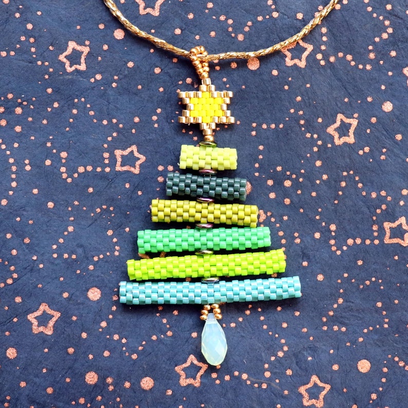 May include: A beaded Christmas tree pendant necklace. The tree is crafted from various shades of green and blue beads, with a yellow star at the top. A gold-coloured chain holds the pendant, and a teardrop-shaped bead hangs below.