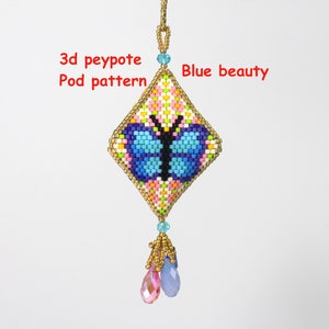 Könnte beinhalten: Ein rautenförmiger Perlenanhänger mit Schmetterlingsdesign. Der Anhänger zeigt einen blauen Schmetterling auf einem Hintergrund aus rosa, gelben und weißen Perlen. Der Text "3d peyote Pod pattern" und "Blue beauty" sind sichtbar. Er hängt an einer goldenen Kette mit hängenden Kristallperlen.