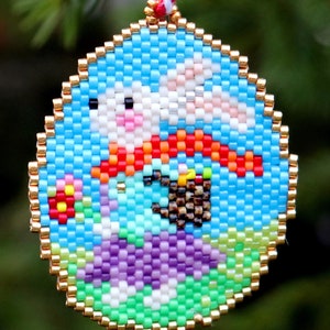 May include: A round beaded ornament featuring a colourful design of a bunny holding a basket of eggs. The bunny is wearing a red scarf and the background is blue with green and purple accents.