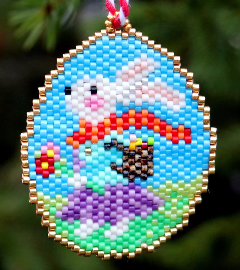 May include: A round beaded ornament featuring a colourful design of a bunny holding a basket of eggs. The bunny is wearing a red scarf and the background is blue with green and purple accents.