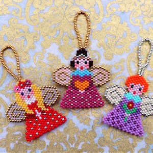 Könnte beinhalten: Drei Perlenengel-Anhänger mit goldenen, rosa, violetten, roten, weißen und blauen Perlen. Jeder Engel hat ein anderes Design und Farbschema.