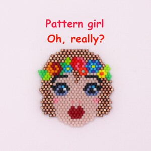 Könnte beinhalten: Ein aufgefädelter Kopf mit blauen Augen, einem roten offenen Mund und einem Blumenkranz. Der Text "Pattern girl Oh, really?" steht über dem Gesicht. Das Gesicht besteht aus kleinen, farbigen Perlen.