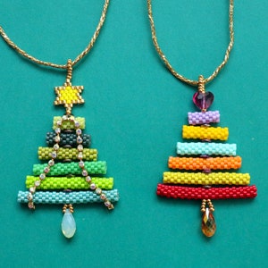 May include: Two beaded Christmas tree pendants on gold chains. One tree is green with a star and crystal accents, the other is rainbow-coloured with a heart and a teardrop gem. The pendants are on a teal background.