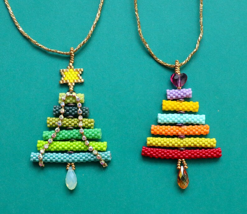 May include: Two beaded Christmas tree pendants on gold chains. One tree is green with a star and crystal accents, the other is rainbow-coloured with a heart and a teardrop gem. The pendants are on a teal background.