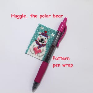 Könnte beinhalten: Ein pinkfarbener Stift neben einem kleinen, rechteckigen, mit Perlen besetzten Kunstwerk mit einem Eisbären mit Hut und Schal, der ein Herz hält. Der Text "Huggle, the polar bear" und "Pattern pen wrap" sind rot.