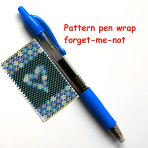 Könnte beinhalten: Ein blauer Stift mit einer Perlenummantelung, die ein Vergissmeinnicht-Blütenmuster zeigt. Das Muster ist in Blautönen, Gelb und Weiß auf einem dunkelgrünen Hintergrund gehalten. Der Text "Pattern pen wrap forget-me-not" ist in Rot über dem Stift geschrieben.