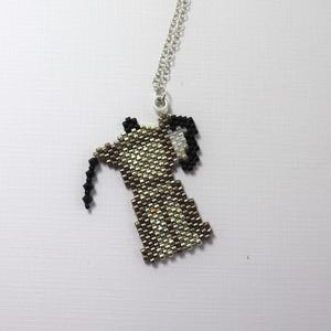 May include: A beaded pendant necklace featuring a coffee maker design. The pendant is made of small, metallic beads in shades of silver, brown, and black. The necklace has a silver chain and a lobster clasp.