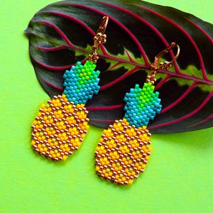 Puede incluir: Un par de pendientes en forma de pi&ntilde;a hechos con cuentas de colores. Los pendientes son de color dorado y tienen un dise&ntilde;o colgante.