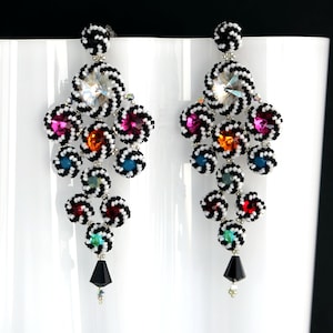 Könnte beinhalten: Ein Paar lange, baumelnde Ohrringe mit schwarzen und weißen Perlen und bunten Kristall-Akzenten. Die Ohrringe bestehen aus verschiedenen Perlen, darunter schwarze und weiße Perlen und bunte Kristalle. Die Ohrringe sind etwa 7,5 cm lang.