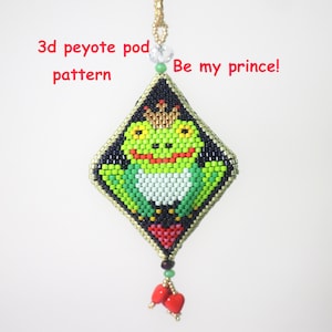 Könnte beinhalten: Ein rautenförmiger Perlenanhänger mit einem grünen Frosch mit goldener Krone, mit dem Text "Be my prince!" und "3d peyote pod pattern". Der Anhänger hat einen schwarzen Rand und rote Herzakzente.