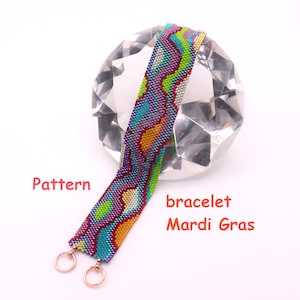 Könnte beinhalten: Ein farbenfrohes Perlenarmband mit einem geometrischen Muster in Lila, Grün, Blau und Gelb. Das Armband mit Mardi-Gras-Thema wird auf einem klaren, facettierten Objekt präsentiert. Das Armband ist etwa 2,5 cm breit.