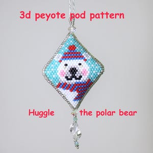 Könnte beinhalten: Handgefertigter, mit Perlen besetzter Eisbären-Ornament mit dem Text "3d peyote pod pattern" und "Huggle the polar bear". Das Ornament zeigt einen weißen Bären mit blau-roter Mütze und Schal vor einem türkisfarbenen Hintergrund.