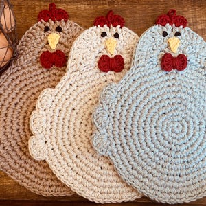 以下が含まれることがあります： 茶色、クリーム色、水色の3色の鶏の形をしたかぎ針編みの鍋つかみ。それぞれに赤い鶏冠と蝶ネクタイ、黄色のくちばし、黒い目があります。鍋つかみは、スカラップエッジのある円形です。