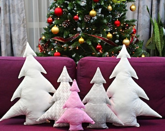 May include: Five decorative Christmas tree pillows in various colors and patterns, including white, pink, and gray, arranged on a burgundy couch with a black and white chevron throw blanket.