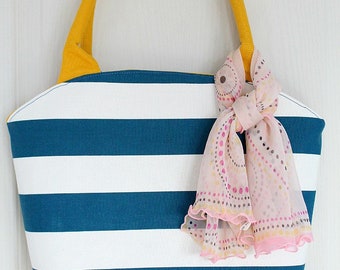 May include: A striped tote bag with a yellow handle and a yellow bottom. The bag is white and teal blue with horizontal stripes. A pink and white patterned scarf is draped over the handle.