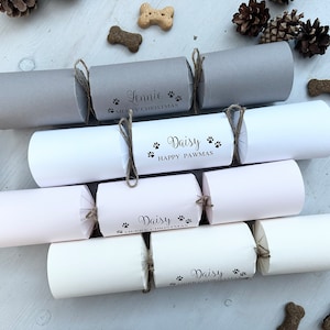 Op de afbeelding: Een set van zes gepersonaliseerde kerstcrackers met een hondenmotief. De crackers zijn versierd met een pootprintontwerp en de namen "Lennie" en "Daisy". De crackers zijn vastgebonden met touw en hebben een feestelijk kerstthema.