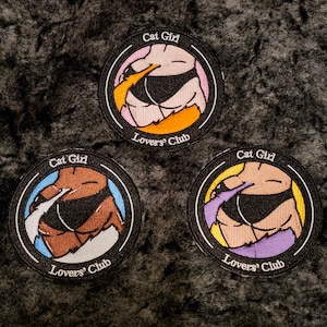 May include: Three round embroidered patches with the text "Cat Girl" and "Lovers' Club". Each patch features a stylized illustration of a figure in a black bikini. The patches have different color schemes, including pink, orange, blue, brown, and purple.