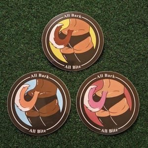 Peut inclure: Trois autocollants ronds avec un dessin de dessin animé d'un torse et d'une queue de chien. Chaque autocollant a une couleur de fond différente : jaune, bleu et rouge. Le texte "All Bark" et "All Bite" est imprimé sur chaque autocollant.