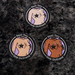 May include: Three circular patches with a black border. Each patch features a stylized torso illustration with a star over the nipple, and the text "Small Titty" and "Goth Girlfriend". Skin tones vary.