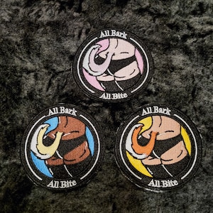 Peut inclure: Trois écussons brodés circulaires avec les textes "All Bark" et "All Bite". Chaque écusson présente une illustration de dessin animé du derrière d'un chien avec un design coloré. Les écussons sont noirs avec des accents blancs et colorés.