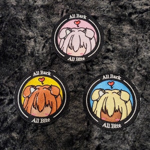May include: Three round embroidered patches with a cartoon dog design. Each patch features a different color scheme: pink, yellow, and blue. The text "All Bark" and "All Bite" are displayed on each patch.